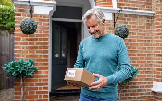 Happy senior man receiving an e-commerce package in the mail at home - lifestyle concepts