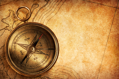 A compass rests on an old generic textured map that shows a nondescript coast line.