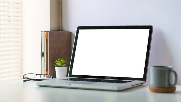 istock Laptop computer with empty display and cup of coffee on white table in bright office interior. 1643302093