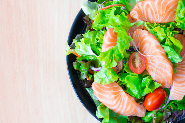 A delightful arrangement of fresh ingredients, including raw salmon, lettuce, tomato, and red cabbage, adorns a rustic wooden table in this top-down view of a salmon salad.