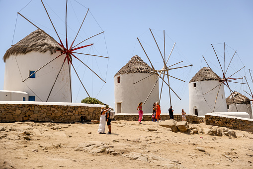 Mykonos, Greece - July 21, 2023: Tourists walking amongst the iconic windmills along the shores of Mykonos Town in Greece