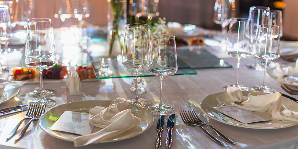 Table setting in a restaurant, close up of forks, knife on a napkin, and empty wine glasses. Served table