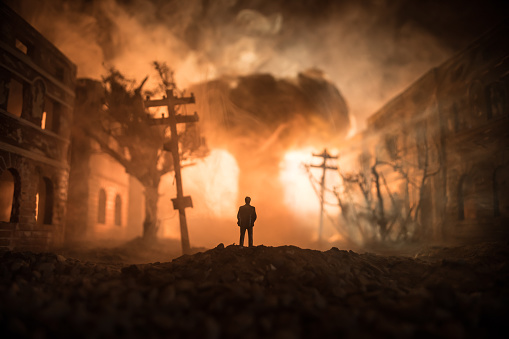 Artwork decoration. A man standing on a road of burnt up city. Apocalyptic view of city downtown as disaster film poster concept. Night scene. City destroyed by war. Selective focus