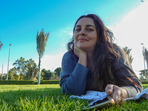 woman lying on the grass in a park looking at the camera