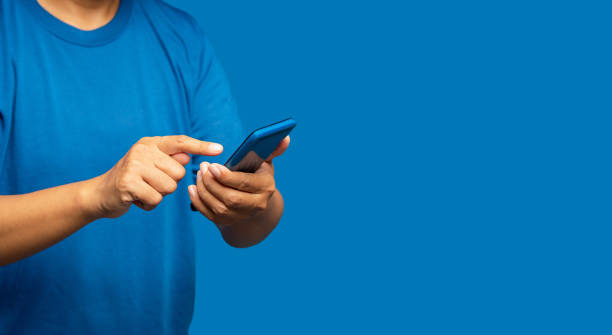 istock Close-up of hands man in a blue casual using a mobile phone while standing on a blue background 1643457296