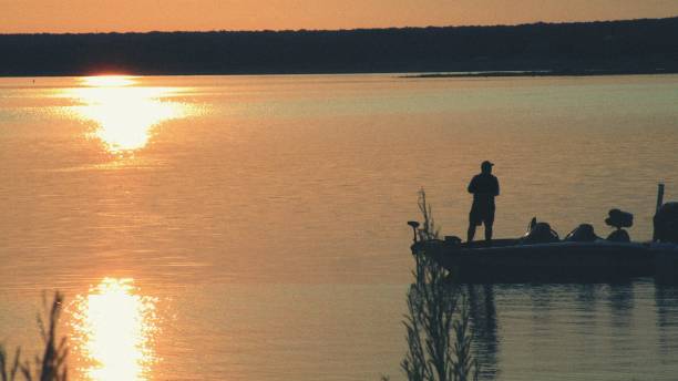 istock Fisherman in Boat Silhouetted Against Lake Sunrise 1643523716