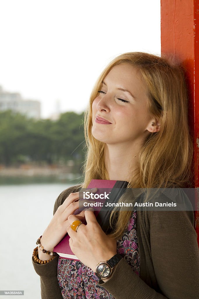 Sognare ad occhi aperti giovane donna tiene un libro vicino al suo petto - Foto stock royalty-free di Acqua