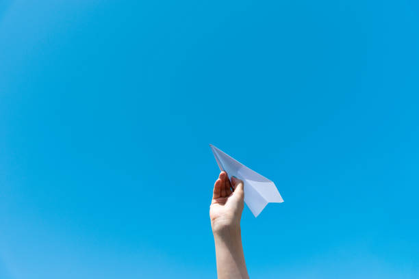 istock Woman hand holding a paper plane under blue sky 1643573985