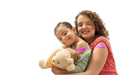 mother and daughter with pink band aid smiling after having an injection. happy mom and kid showing vaccine plaster bandage. hispanic woman and child looking to camera, isolated on a white background