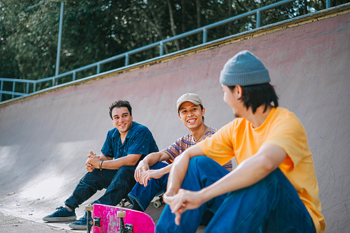 3 skateboarders resting in skateboard park after practicing talking