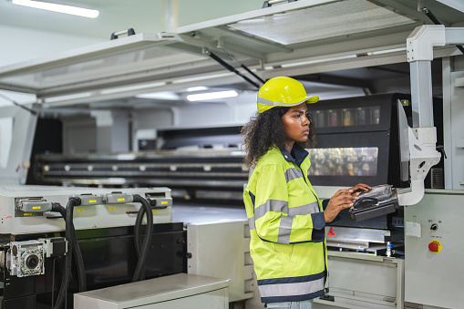 African American Female Engineer Mastering Manufacturing Machinery, Efficiency and innovation converge as this talented woman engineer guides the manufacturing process with technical finesse.