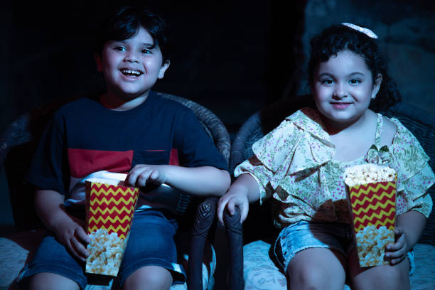 des enfants indiens heureux portant des lunettes 3d mangeant du maïs soufflé et riant assis et regardant un film au cinéma. - friends television show photos et images de collection