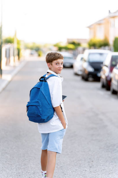 istock Young boy with backpack looking at camera while walking on the street. 1643695410