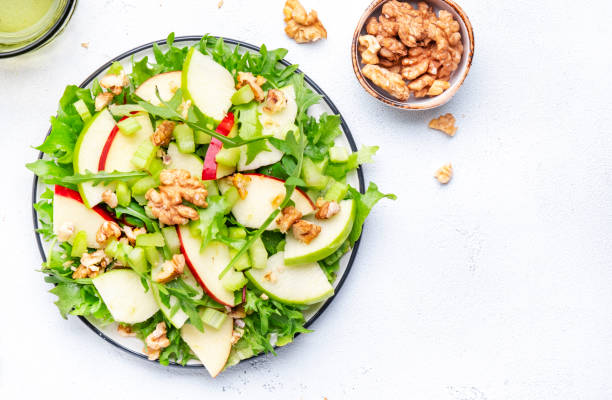 istock Waldorf salad with apples, green celery, lettuce, arugula and walnuts on plate, white background, top view 1643695612