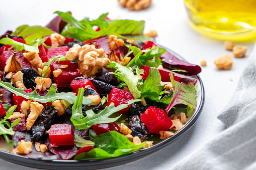 Healthy vegan salad with beet, dry prunes, arugula, swiss chard and walnuts, white table background. Fresh useful vegetarian dish for clean eating