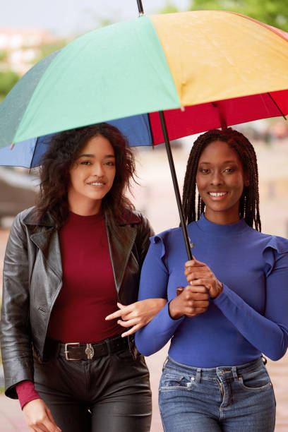 istock Two women looking at camera and smiling while standing with an umbrella outdoors. 1643703082