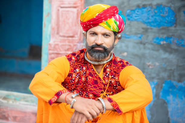 portrait d’un homme heureux traditionnel du nord de l’inde portant une tenue colorée assis. homme souriant du rajasthan avec turban et tenues ethniques. culture et mode. regarder la caméra - asian tribal culture photos photos et images de collection