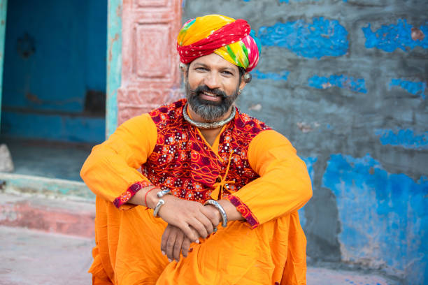 portrait d’un homme heureux traditionnel du nord de l’inde portant une tenue colorée assis. homme souriant du rajasthan avec turban et tenues ethniques. culture et mode. regarder la caméra - asian tribal culture photos photos et images de collection