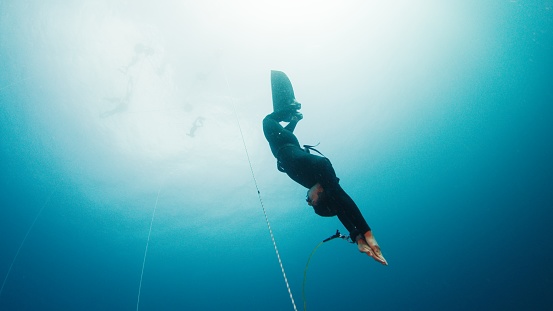 Freediving on the rope in a sea. Male freediver descends along the rope in monofin