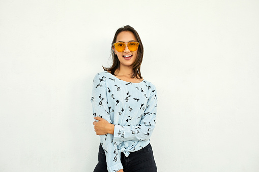 Portrait of happy young businesswoman wearing sunglasses. Cheerful female professional is against white background. She is in casual.