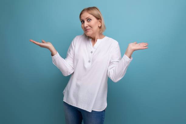 affascinante donna dai capelli biondi ben curata di anni maturi con pelle uniforme su uno sfondo di studio - women mature adult 50 55 years 50s foto e immagini stock