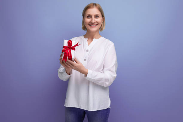 istock blond mature woman holding gift box on studio background 1643800469