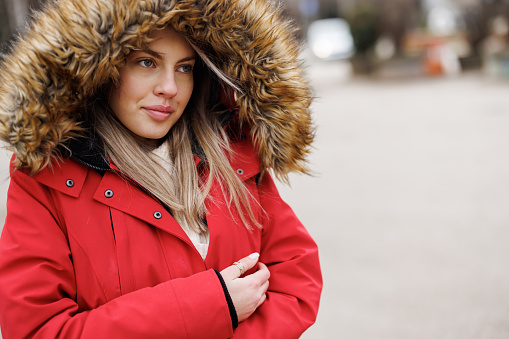 Beautiful young woman in red hooded jacket walking outdoors