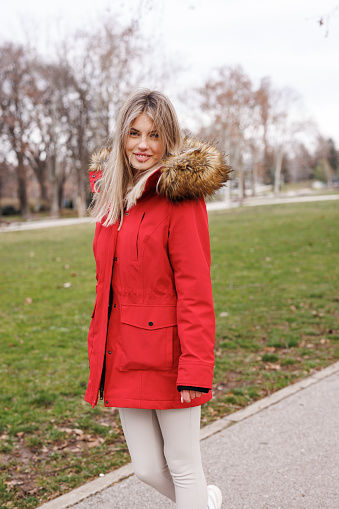 Portrait of beautiful young woman in red  jacket standing and looking at camera outdoors