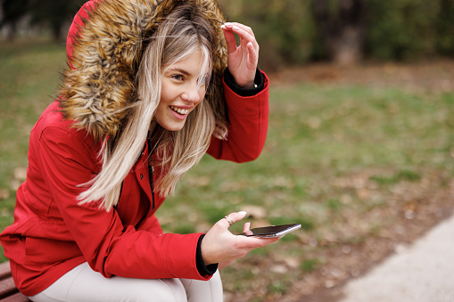 Smiling young woman sitting and texting on bench in park