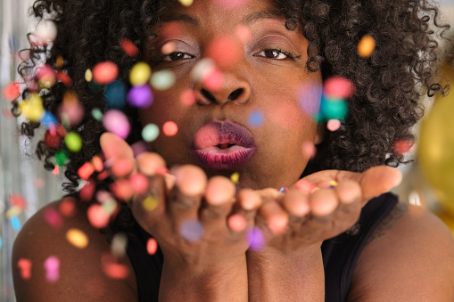 African woman blowing confetti from hands. Celebration and event concept.