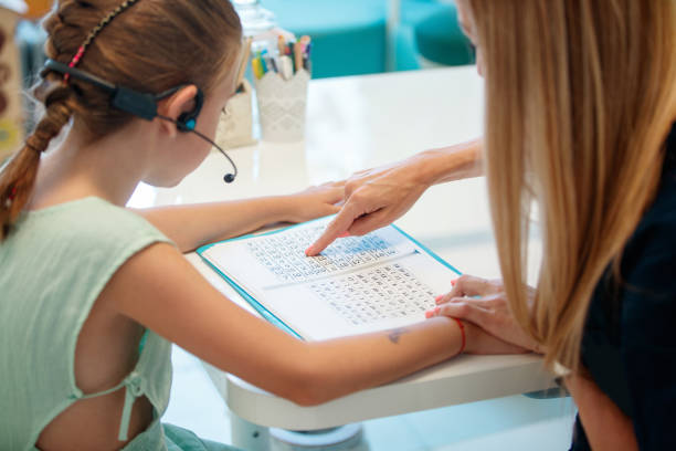 Girl wearing headset and reading assisted by specialist at speech therapy Girl wearing headset and reading with guidance of female doctor at the appointment, speech therapy techniques and technology assistive technology stock pictures, royalty-free photos & images