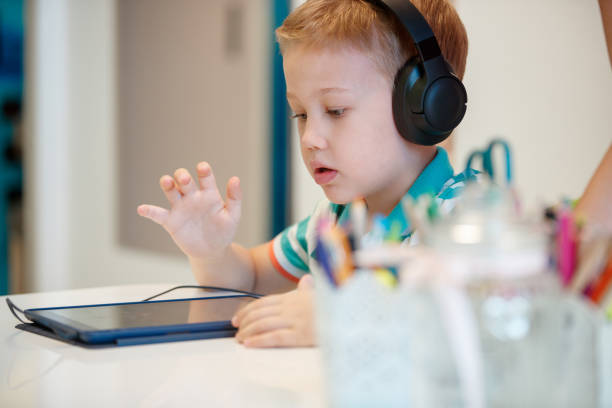 Preschool boy wearing headphones and using tablet at speech therapy stock photo
