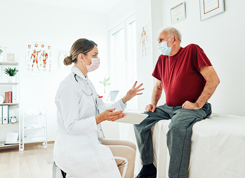 Portrait of a female doctor holding a tablet and senior patient wearing protective masks at her doctor's office in clinic