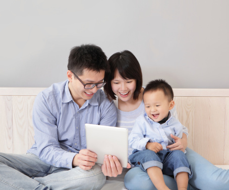 A happy, family sitting on bed at home having fun using a tablet computer pc, asian people