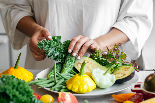 Woman's hands lay out fresh vegetables and herbs on a plate on the kitchen table, healthy eating, organic products.