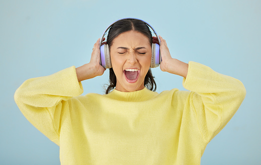 Music, screaming and headphones with a woman in studio on a gray background while streaming audio. Radio, shouting or expression and an attractive young female listening to sound with her eyes closed