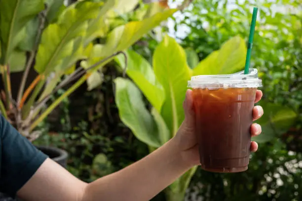 Photo of Cropped shot view of woman hand holding a plastic cup of iced Americano.