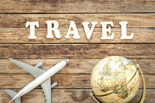 The word Travel composed of wooden letters, airplane and globe on a wooden background, top view.