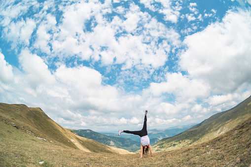 The young woman does acrobatics and fitness exercises in nature, in a beautiful mountain landscape.