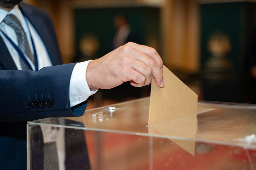 Close up of man hand voting at ballot box.