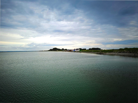 stormy weather is getting closer on a summer day. Dark clouds clashing with the sunny blue sky. View from the bathing bridge over the quiet water in the bay