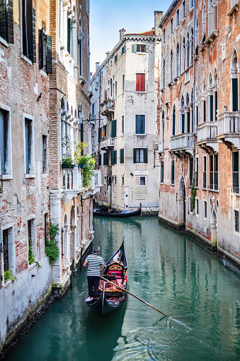 Canal in Venice, Italy with gondolier rowing gondola. Romantic Venetian waterway