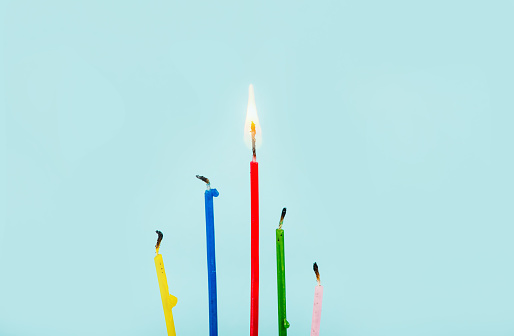 One candle burning and others are put out on blue background with lot of copy space. Concept of the best.