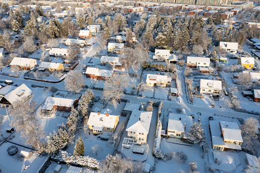 From an elevated drone's bird's-eye view, the expansive residential district unfolds beneath, completely enveloped in a fresh blanket of snow. Streets, homes, and trees wear their wintry coat, creating a breathtaking panorama that captures the sheer tranquility and ethereal beauty characteristic of a pristine winter landscape.