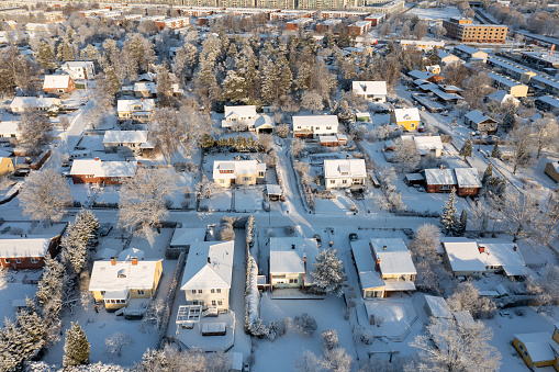 Seen from a drone's aerial perspective, the residential area is covered in a pristine layer of snow, capturing the serene beauty of winter. Apartment buildings are visible in the distance, adding layers to the tranquil scene.