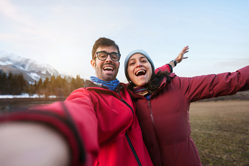 Young hispanic couple on red winter clothes taking selfie picture in the mountain