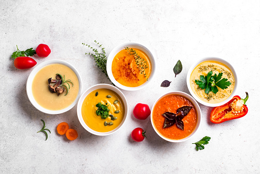 Autumn soups. Set of various seasonal vegetable soups and organic ingredients on white background. Homemade colourful seasonal vegan soups.
