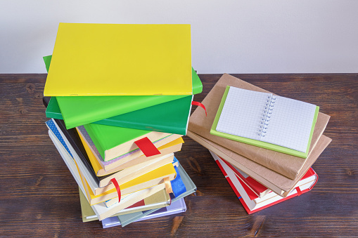 Stacks of different multicolored books  and open notepad on dark rustic table. Copy space