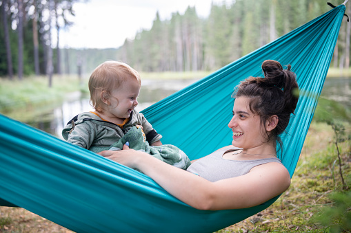 Happy young mother and her baby boy relaxing on a hammock in nature on wild camping.