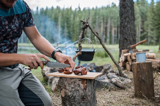 Man on wild camping cutting steak.